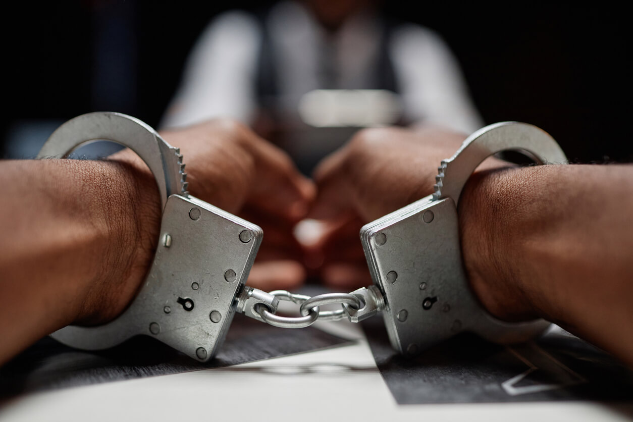 close up of man wearing handcuffs on hands, criminal suspect
