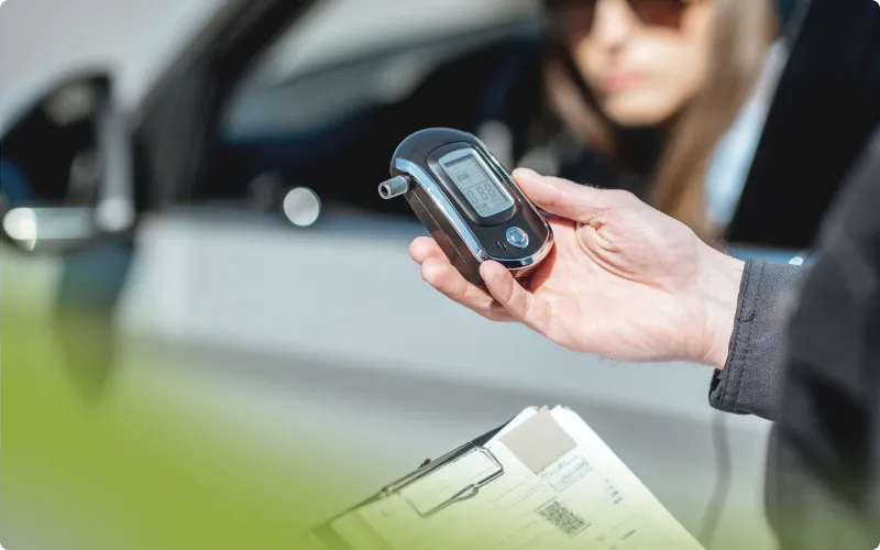 Officer holding a breathalyzer device up to a driver at a car window